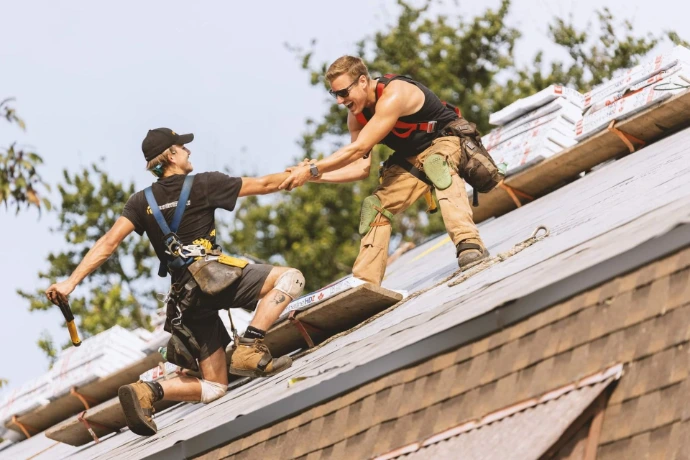Deux couvreurs travaillant en équipe sur un toit escarpé.